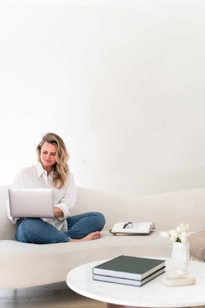 a woman sitting in cross legged on a couch with a laptop on her lap
